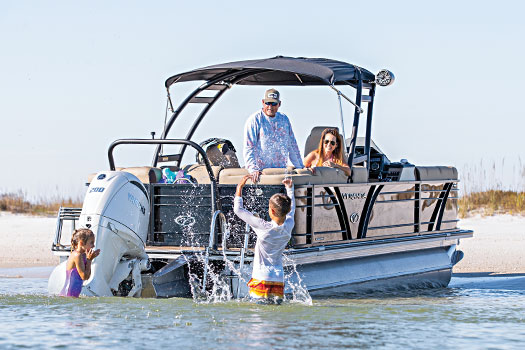 Two kids play in the water while their parents look on from their boat.