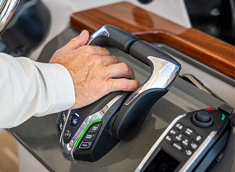 A hand operating a boat's joystick docking control at the helm console.